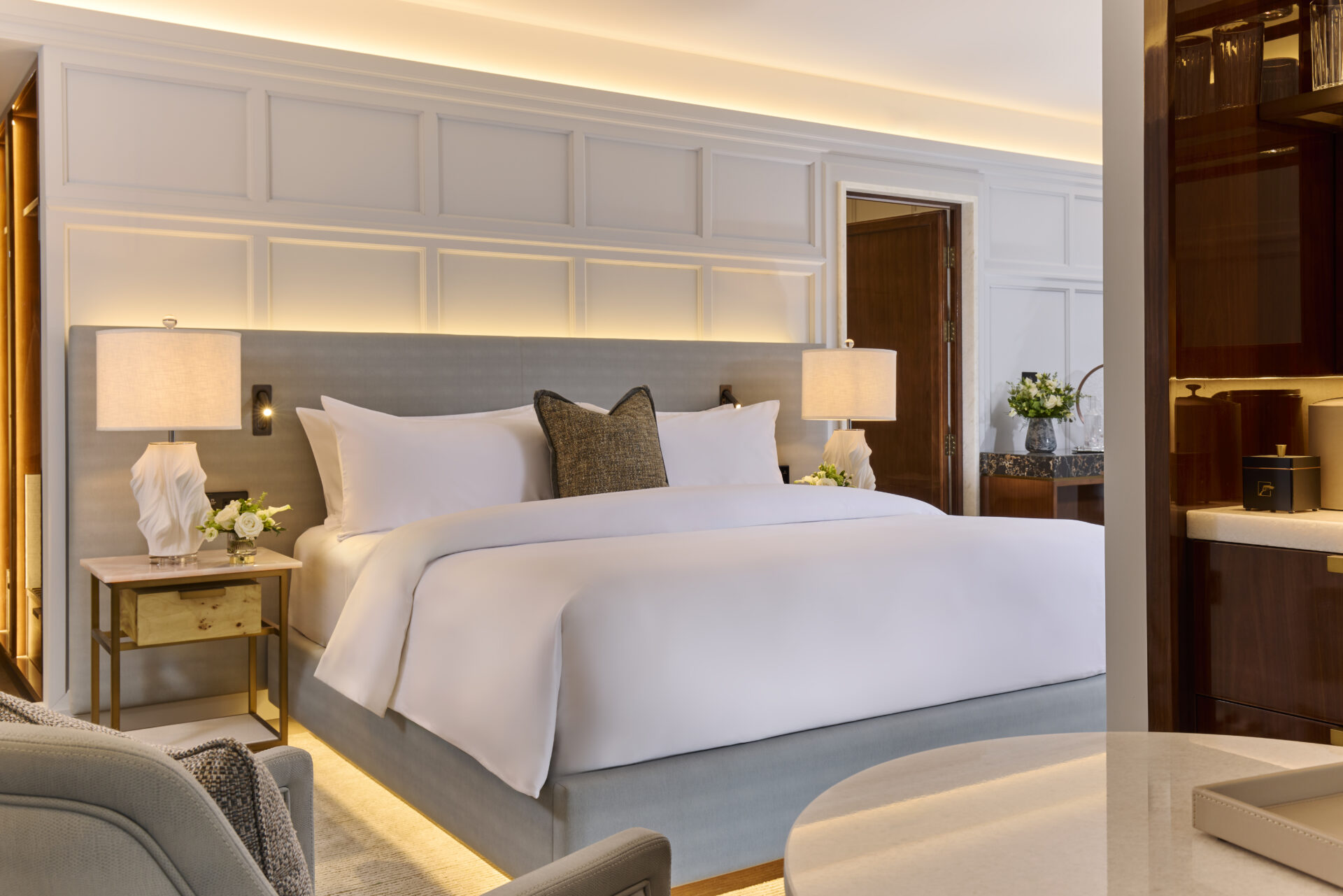 Elegantly appointed king suite at The Hawthorn by Galway Bay, featuring crisp white linen, an olive accent cushion, sculptural table lamps, gold-toned nightstands, fresh flowers and rich timber wardrobe detailing
